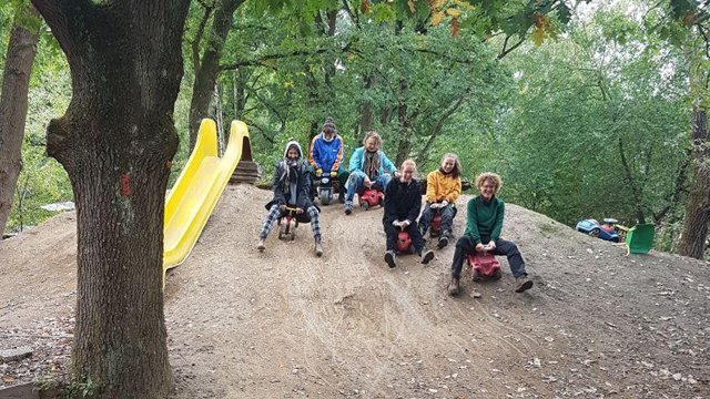 Betreuer fahren mit Bobbycars den Lehmhügel herunter