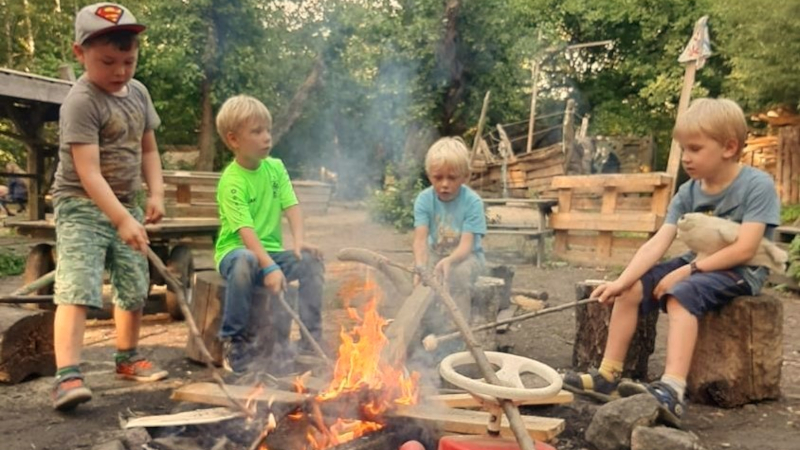 Kinder sitzen am Lagerfeuer und machen Stockbrot