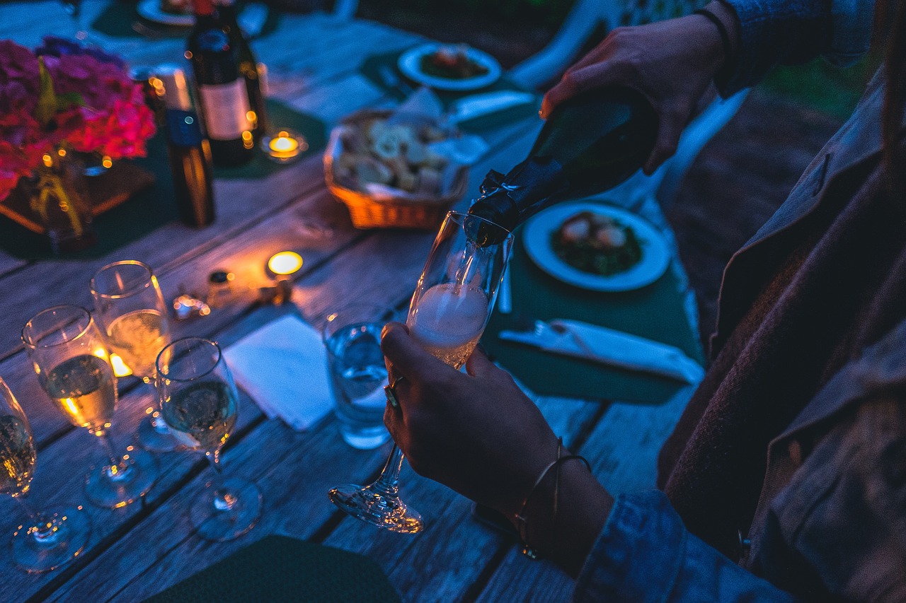 Gartentisch mit Sektgläsern, Kerzen und Essen, Es wird Sekt eingeschenkt